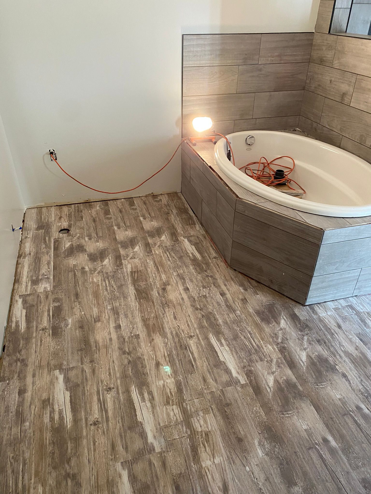 Bathroom tub installation with wood-look tile surround and luxury vinyl plank flooring